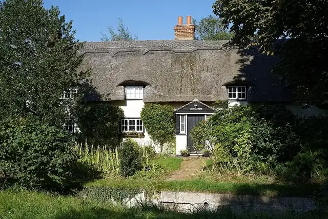 A thatched cottage behind a green summer garden